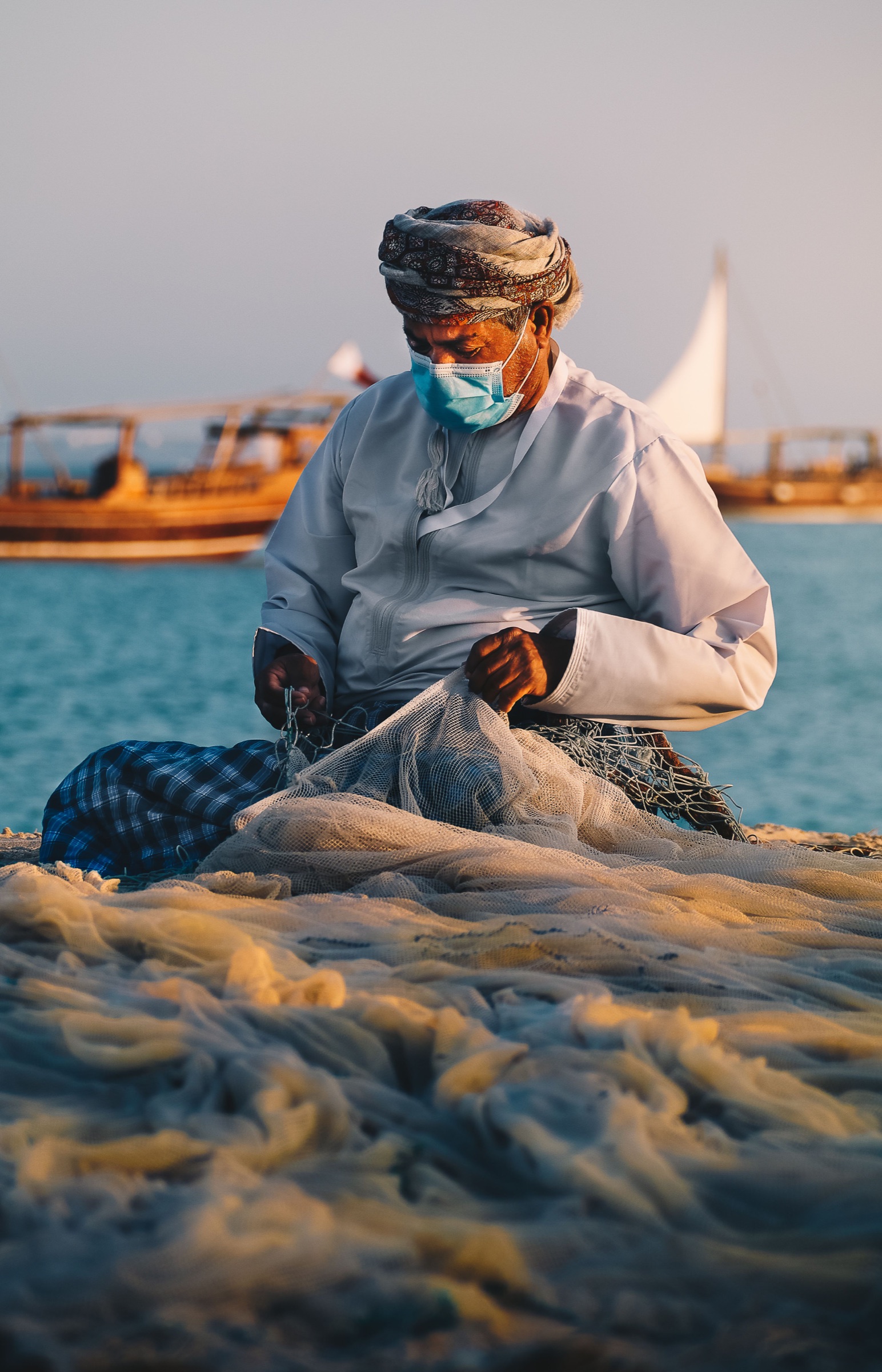 Omani fisherman repairing a net beside traditional boats